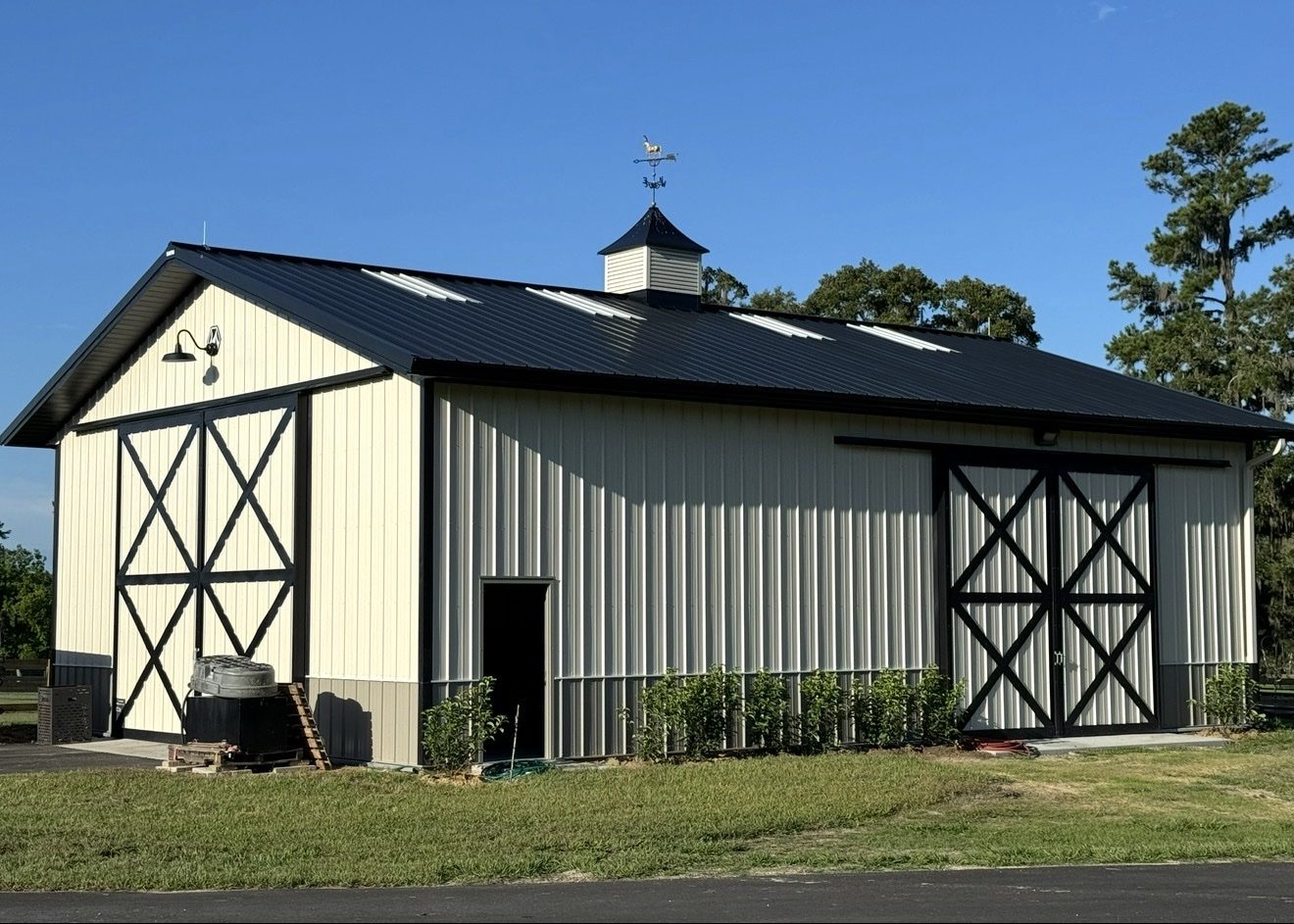 Cream-colored horse barn with a cupola and fenced paddocks in front